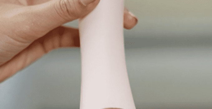 Womens hands holding a light pink vibrator