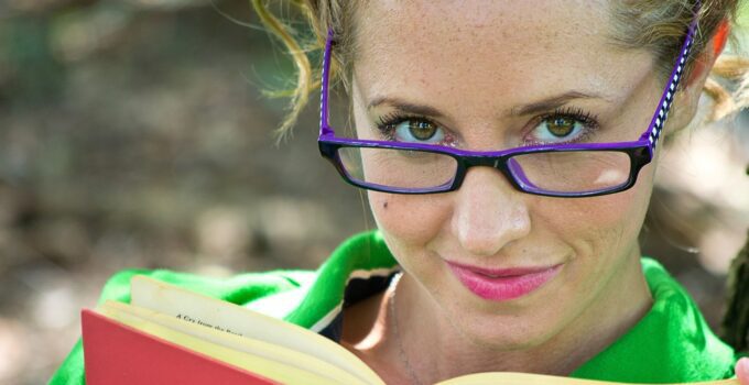 A girl wearing purple rimmed glasses and a green top reading a book in the article