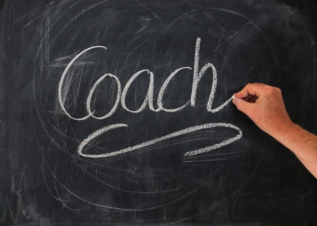 A blackboard with a hand writing coach in large letters with chalk on the board. Used in the article What is a Career Coach?