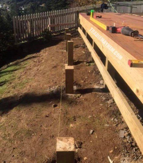 A timber deck with a timber fence in the background. On the deck are some builders tools. In front of the deck is 5 posts that are out of line. Used in the article Why are Landscaping Businesses Unprofitable?