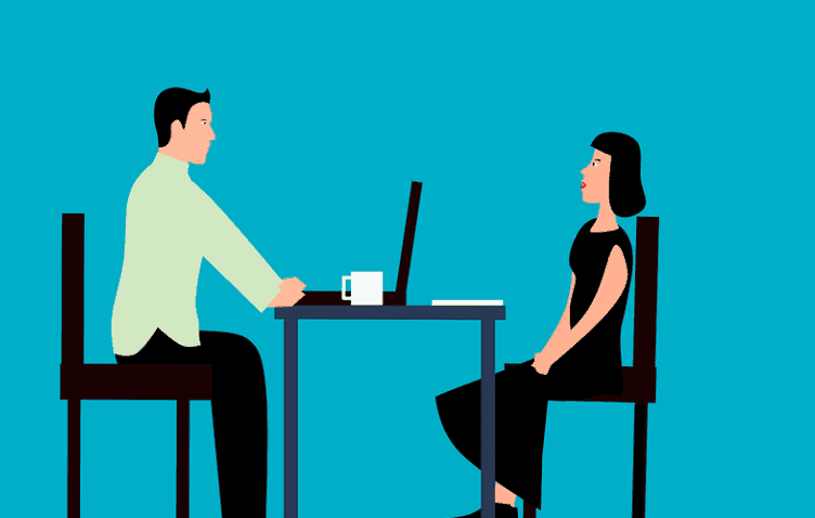 An animation of a man interviewing a woman for a job. A cup of coffee is on the desk beside an open laptop. used in the article, Can you be Re-hired after Being Fired?