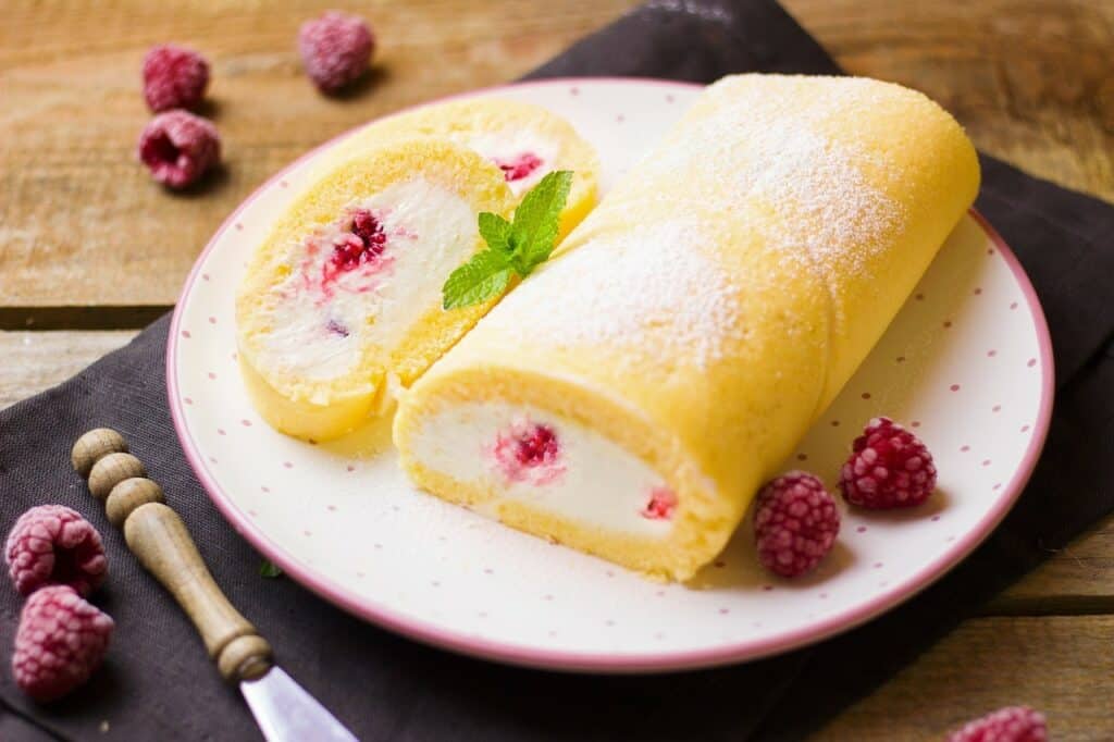 A roulade cake on a plate with a mint leaf on a slice and raspberries alongside the cake and beside the knife used in the article The 5 Biggest problems facing bakeries.