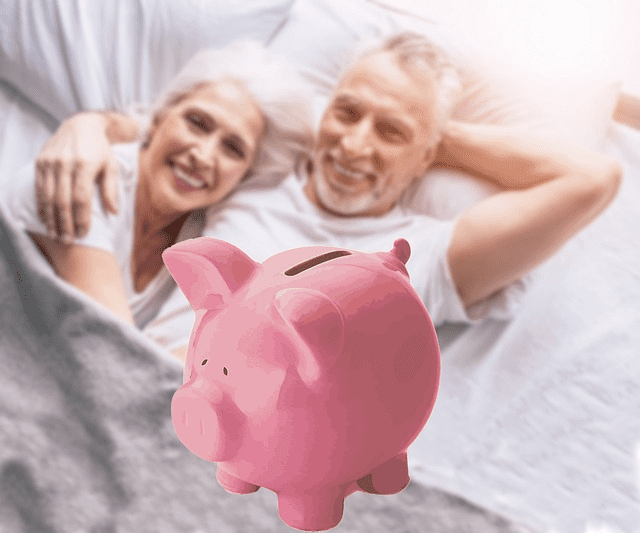 A retired couple in bed with a pink piggy bank in the foreground. Used in the article 7 profitable retirement hobbies for couples to turn passions into income. 
