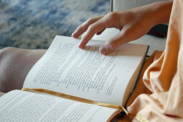 An open book on the leg of a woman reading the text using her hand to guide her through the paragraphs. Used in the article: Online Education for stay-at-home Parents. 