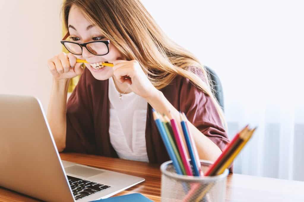 Student at a Laptop with a pencil between her teeth, her hands gripping the pencil as if she is about to break it. Used in the article 5 Proven Strategies to Turn Your Online Study Stress Into Success!
